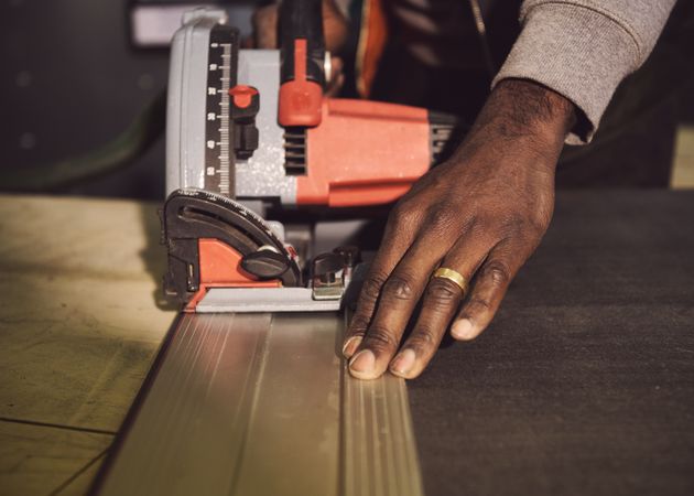 Hands of a Black male designer cutting material with saw