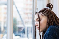 Pensive woman with dreadlocks looking out the window