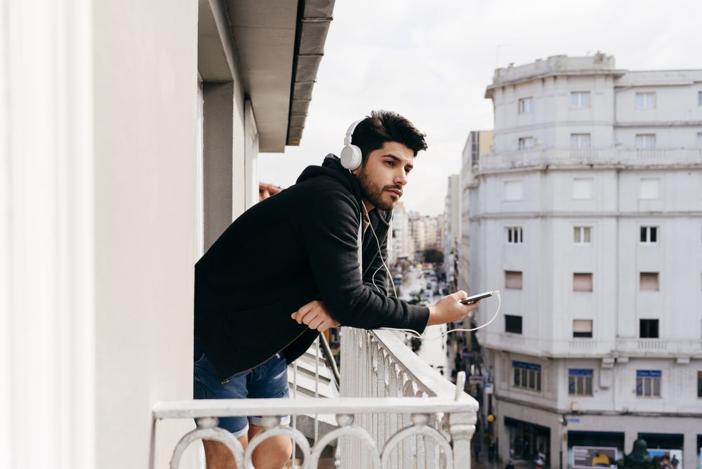 Young happy man holding smartphone on balcony