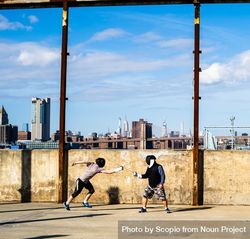 Two people fencing in Brooklyn Bridge Park, with the Empire State Building in the distance 4Aonm0