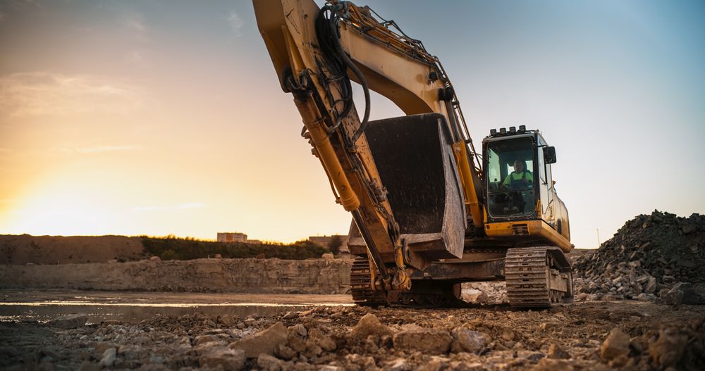 Construction Site On Sunny Evening: Industrial Excavator Driving To Complete Work Tasks Related To Building New Real Estate Project. Man Operating Heavy Machinery To Build New Apartment Complex.