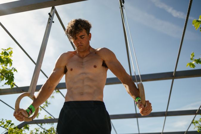 Strong young sportsman exercising with rings