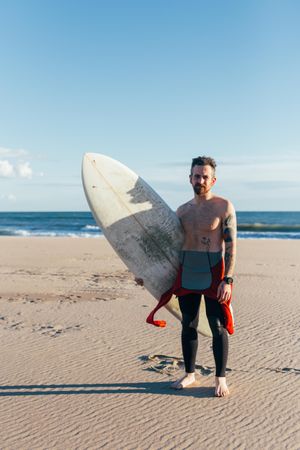 Portrait of man in wetsuit with surfboard, vertical