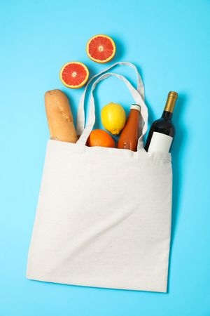 Eco bag with bottle of wine, juice, fruits and baguette on color background, space for text