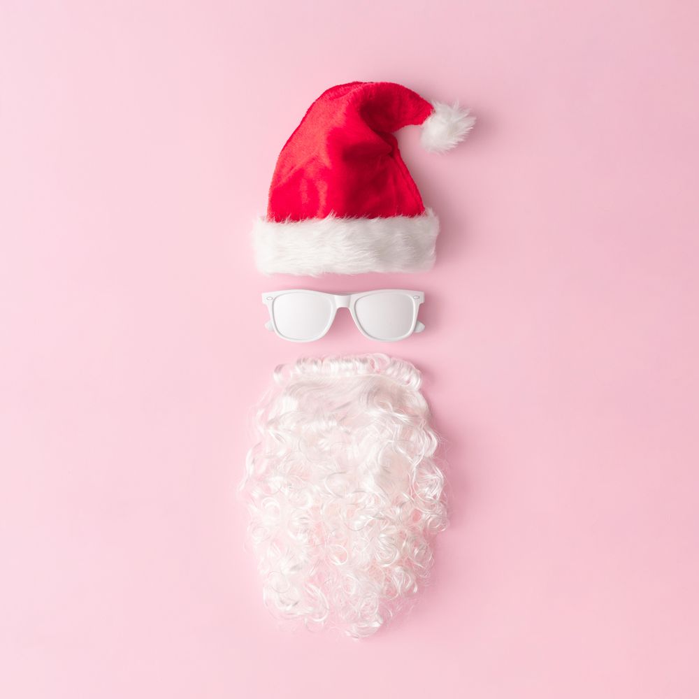 Santa face made of sunglasses, hat and beard on pink background
