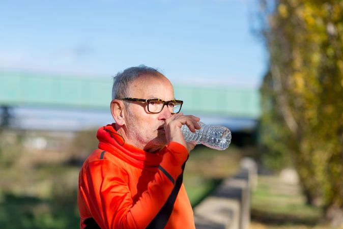Older male in glasses drinking from water bottle outside