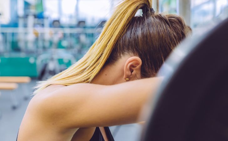 Woman resting head on barbell between tough sets