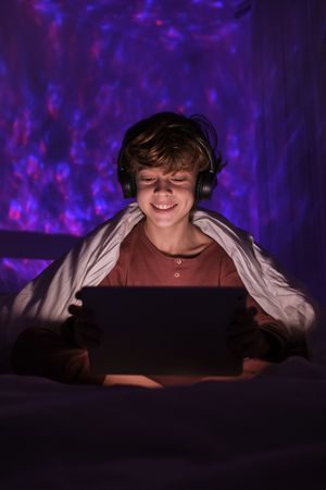Boy in headphones browsing tablet in darkness