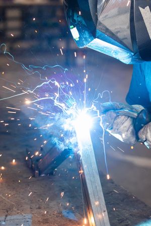 Welder in protective helmet welding metal detail in workshop