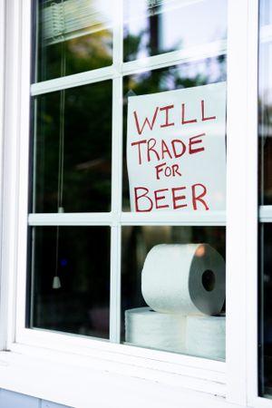 Angled view of funny sign in window of house asking for beer in exchange for toilet paper