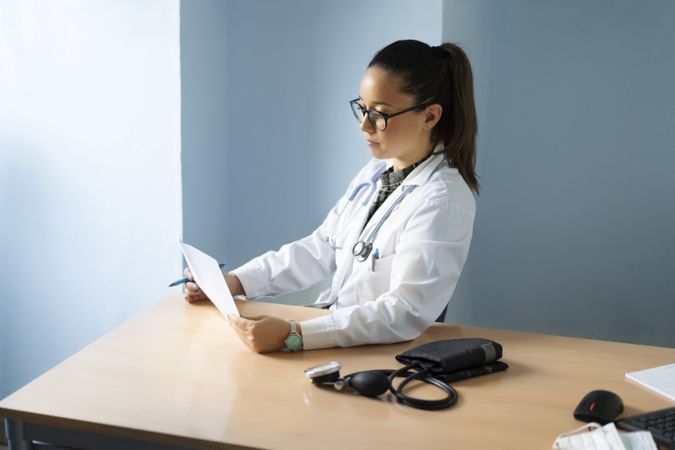 Young doctor with document at table near pulsometer