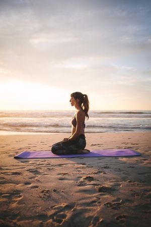 Side view of fitness woman sitting in yoga pose at beach