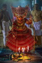 Man performing Theyyam ritual form of dance worship surrounded by men 5oKXz5
