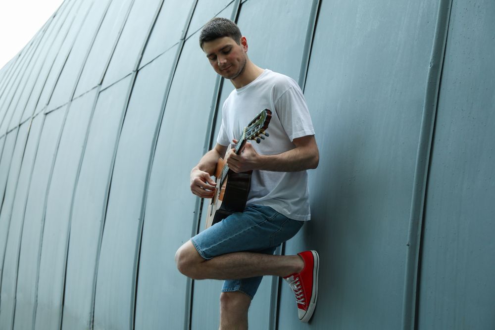 The young man leaned on the wall and play on guitar