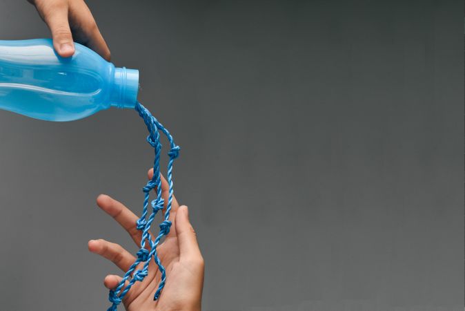Blue bottle with rope pouring out into person’s hand
