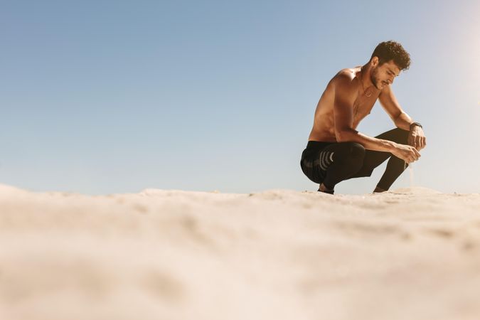 Man bending down and taking a break during workout at the beach