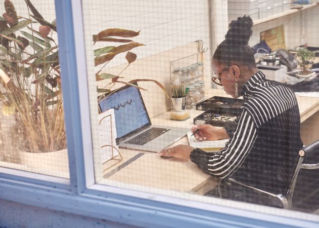 Woman working on laptop shot through window
