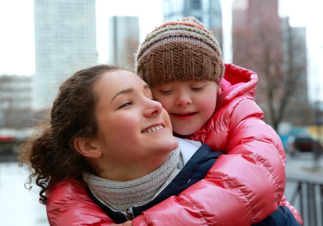 A young girl with Down syndrome on her smiling sister’s back