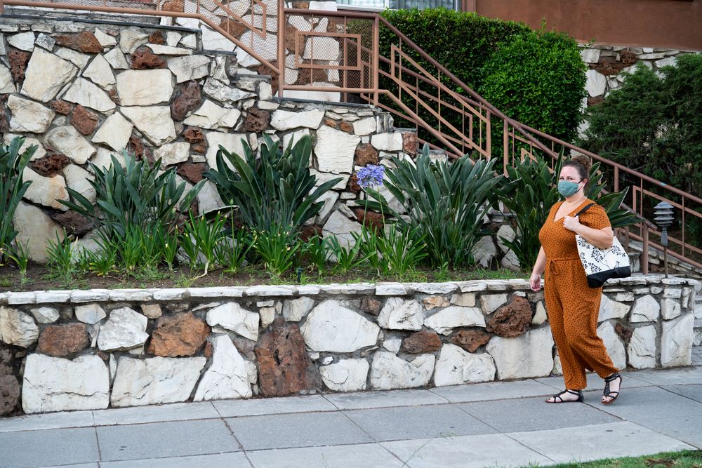 Woman walking down sidewalk carrying tote bag and wearing a mask