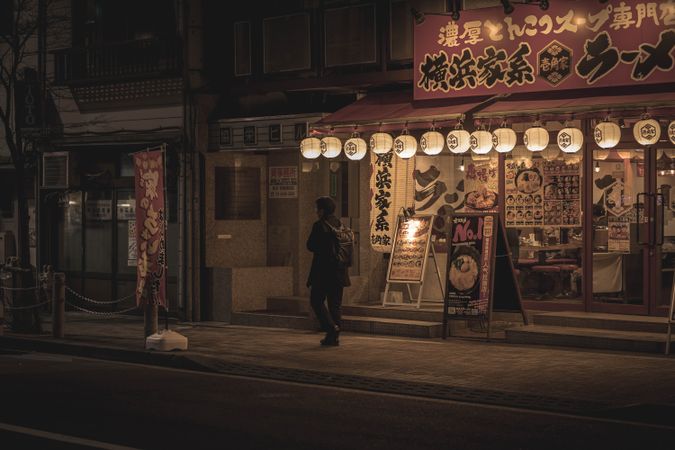 Man in dark coat walking on sidewalk at night in Japan