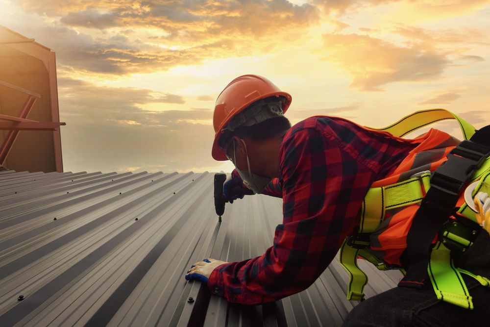 Man with bump cap drilling a screw into metal bar at the rooftop at sunset
