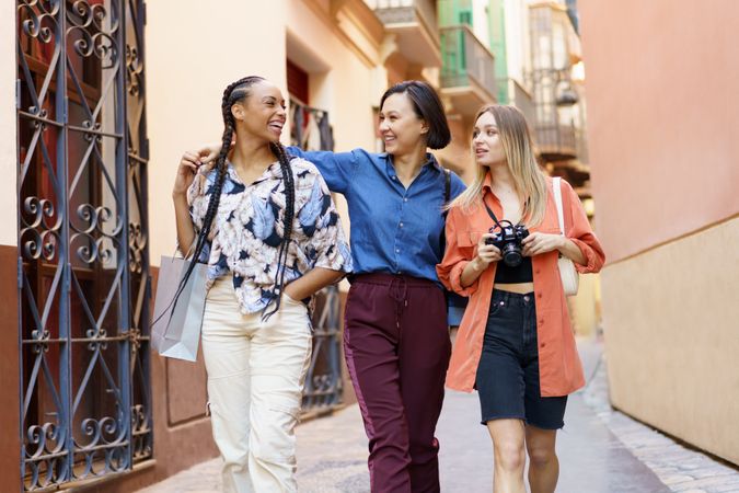 Three laughing women strolling down narrow lane with camera