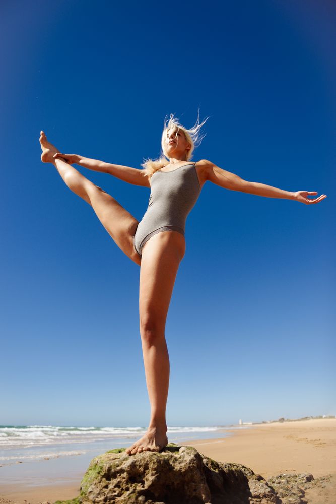 Woman balancing in yoga pose on rock at the seaside