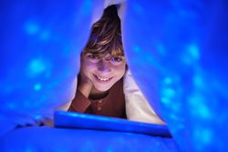 Delighted boy surfing tablet under blanket at night