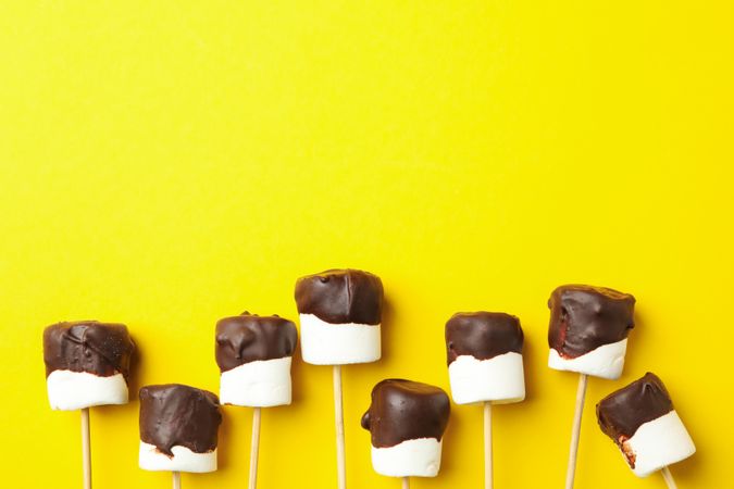 Marshmallows in chocolate on yellow background, space for text