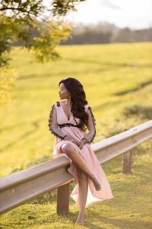 Woman in pink dress sitting on rail in green grass field