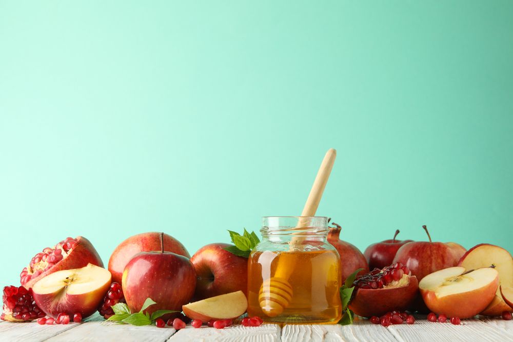 Fresh pomegranate, apples, pot of honey with dipper on mint background, copy space