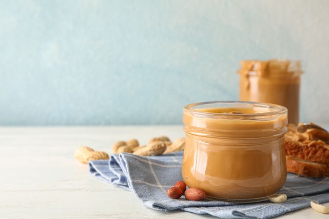 Glass jar with peanut butter, peanut, kitchen towel, spoon and peanut butter sandwich on wooden background, space for text