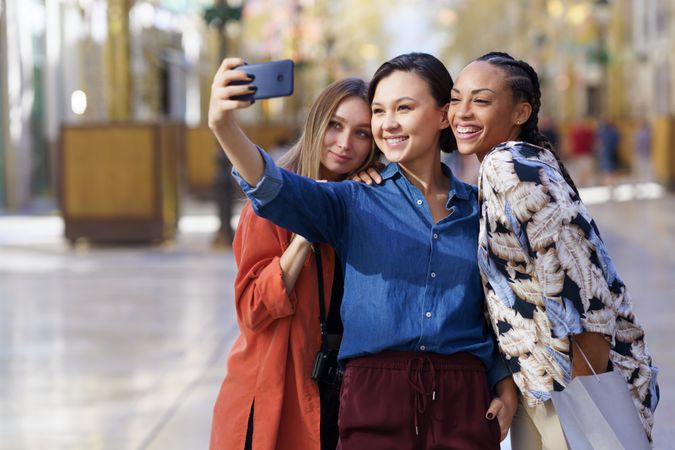 Three smiling women taking selfie with phone in city