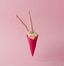 Doll legs emerging from vanilla ice cream in pink waffle cone on pink pastel background