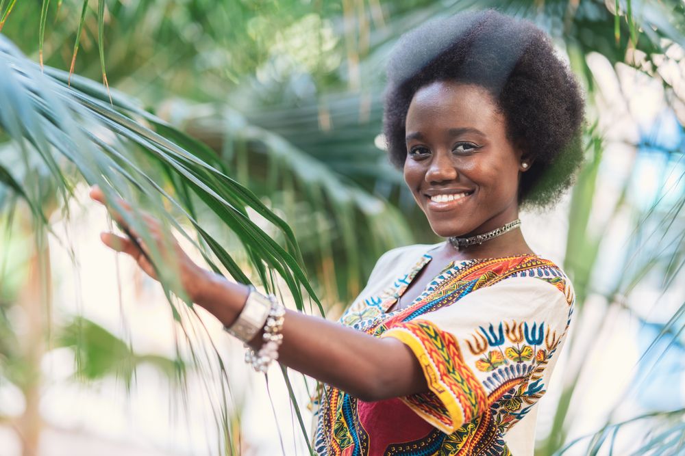 Cheerful Black woman  amidst palm leaves