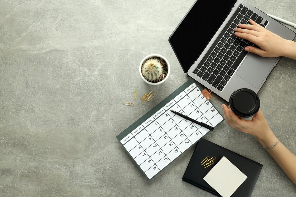 Top view of a person at a grey desk with calendar, laptop, cactus and coffee