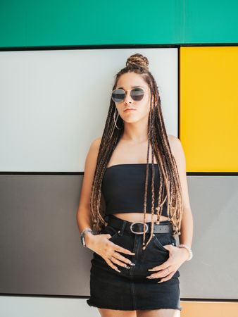 Charming teenage girl with dreadlocks in sunglasses nearby colorful wall