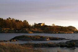 Rocky shore with house of tranquil sea in dusk