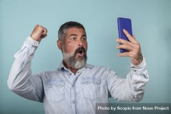 Excited man holding smartphone against blue background 4dWka5