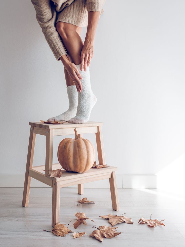 Crop female in socks on ladder with pumpkin