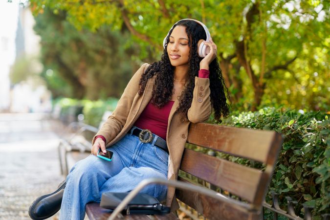 A Young Woman Sitting on a Bench, Enjoying Music in a Peaceful Park Setting, Relaxing