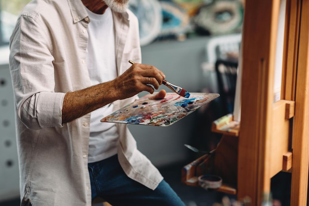 Man dipping painter in blue paint on palette