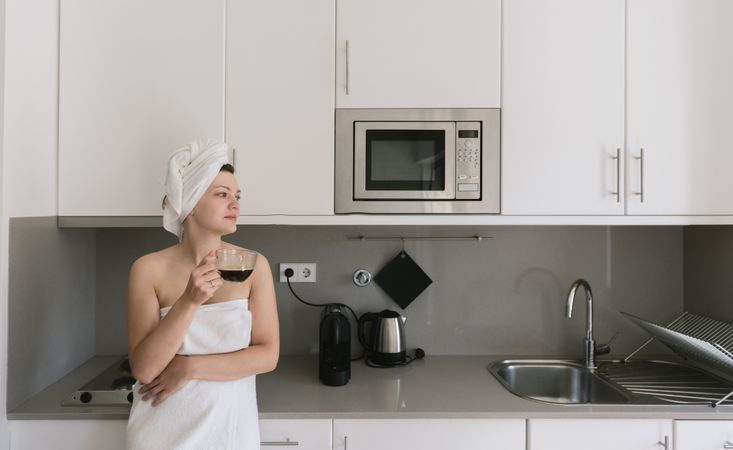 Joyful adult woman enjoying day off while having hot drink after bath in apartment with simple interior design