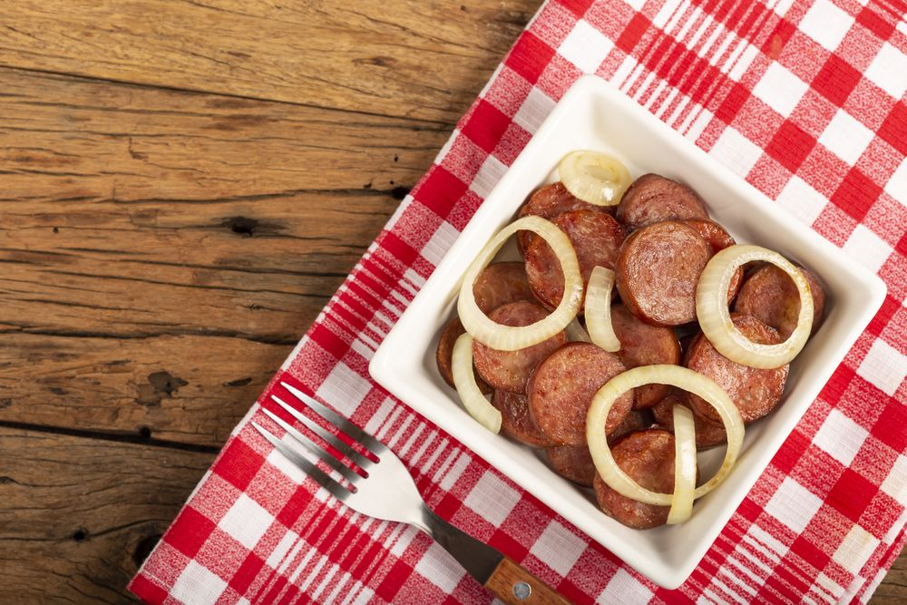 Sliced calabrese sausage with onion on wooden background.