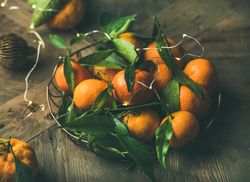Freshly picked tangerines with leaves in wire bowl on wooden table