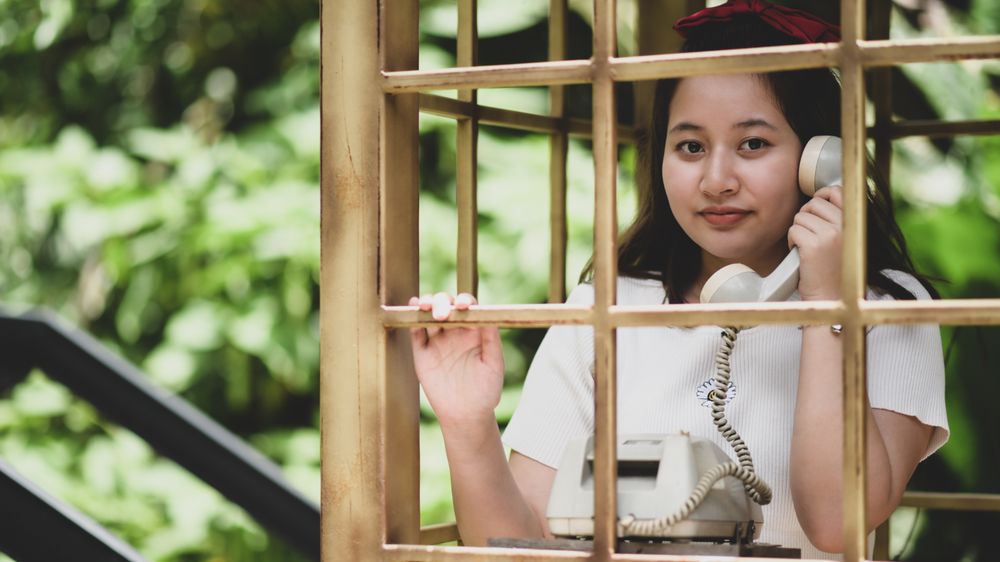 A smiling woman posing with a classic phone while traveling, she smiles.