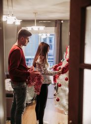 Young couple expecting baby arranging Christmas tree at home