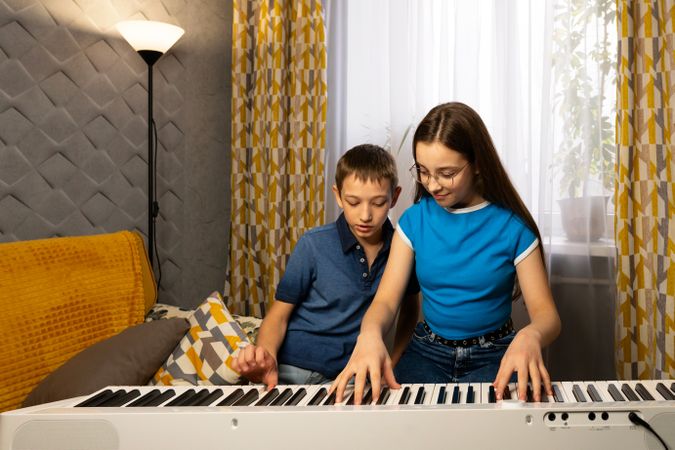 Two kids focus on playing digital piano in living room.