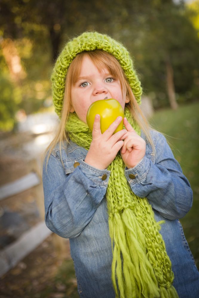 Young Girl Wearing Green Scarf and Hat Eating Apple Outside