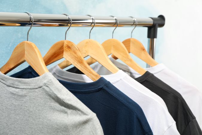 Rack with blank t-shirts on blue background, close up